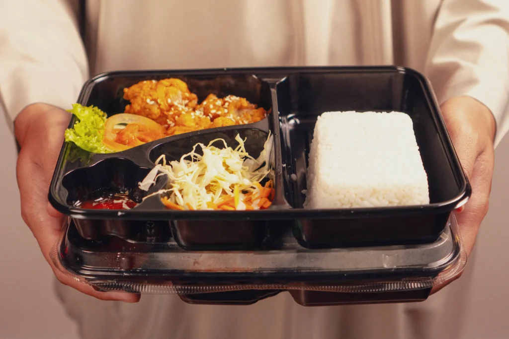 Kucharz trzymający świeże dania na wynos w pudełkach typu lunchbox